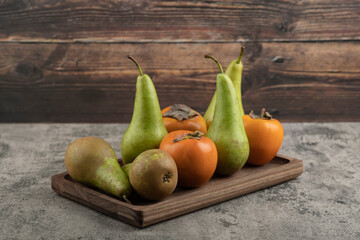 Delicious fuyu persimmons and ripe pears on wooden plate