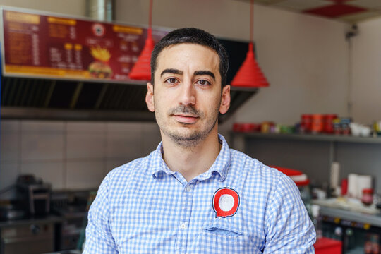 Front View Portrait Of Adult Caucasian Man Standing At Work In Cafe Bar Or Restaurant Grill - Young Serious Entrepreneur Small Business Owner Front View Portrait Real People Concept