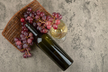 Wicker basket of red grapes with glass of white wine on marble table