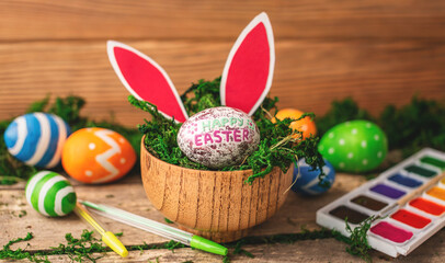 Bright colorful Easter eggs and rabbit ears on a wooden background covered with green moss