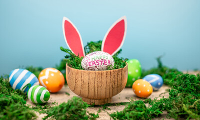 Fototapeta na wymiar Bright colorful Easter eggs and rabbit ears on a blue and wooden background with green moss