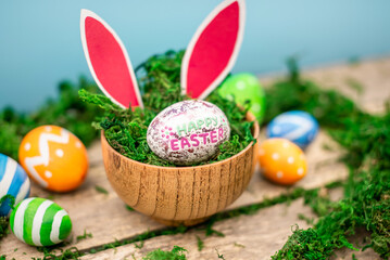 Bright colorful Easter eggs and rabbit ears on a blue and wooden background with green moss