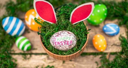 Bright colorful Easter eggs and rabbit ears on a wooden background covered with green moss