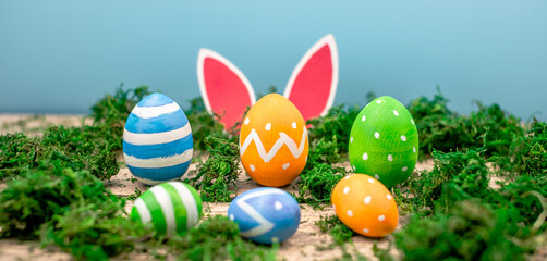 Bright colorful Easter eggs and rabbit ears on a blue and wooden background with green moss
