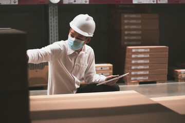 Soft focus asian engineer or technician wearing mask,safety hard hat,uses digital tablet check merchandise stock,security cargo management,in warehouse,industry business  logistic and export concept