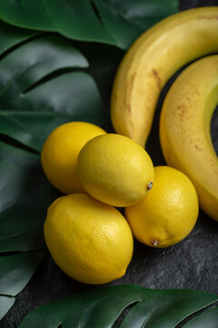 Close up photo of lemons and bananas over black background with green leaves