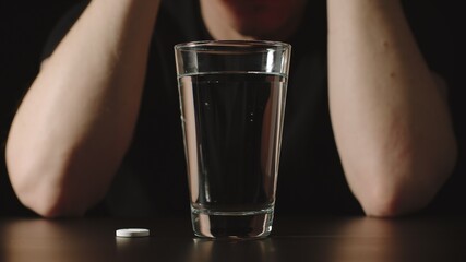 Man sitting in front of a glass and a pill on the table - 416864477