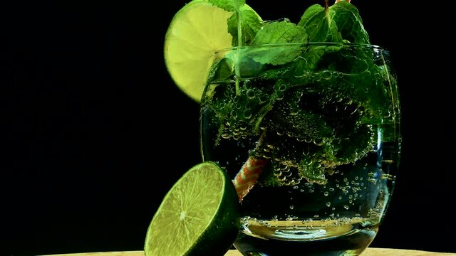 Alcohol with mojito in a transparent glass on a black background, summer drink, put a straw in a glass, a refreshing drink with mojito and lime.