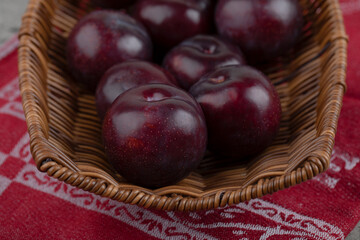 A wicker basket with fresh healthy purple plums on stone background