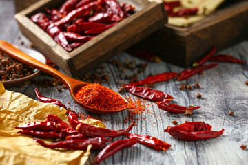Chili powder in wooden spoon and dry pepper on grey wooden table