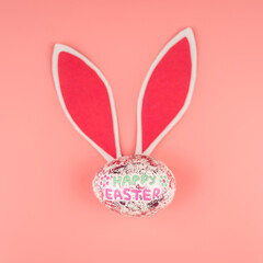 Shiny Easter egg with paper rabbit ears on a pink background. Top view