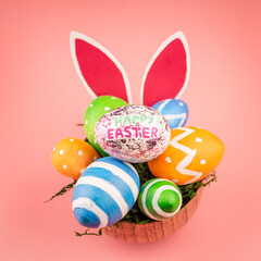 Bright Easter colorful eggs in a wooden bowl, paper rabbit ears on a pink background