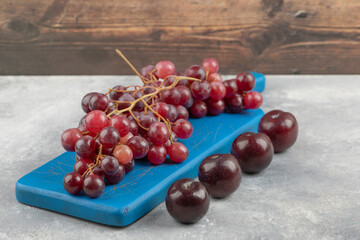 Red grapes on blue cutting board with fresh plums on marble surface