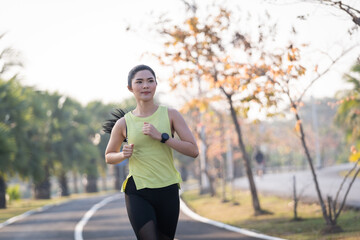 A young Asian woman runner athlete in sports outfit jogging and workout in the city park in the morning. Healthy lifestyle young sporty asian woman running at tropical park. Sport and recreation