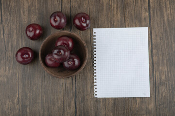 A wooden bowl of fresh purple plums with sheet of paper
