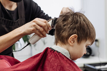 Close-up of woman hands grooming kid boy hair in barber shop.