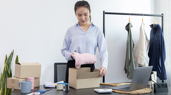 Young Asian women pack their clothes into boxes and prepare them to be delivered by post, Online clothing sales business, Business of selling clothes on social media or selling online.