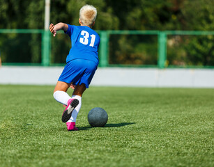 Obraz premium Young sport boys in blue sportswear running and kicking a ball on pitch. Soccer youth team plays football in summer. Activities for kids, training 