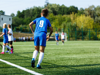Obraz premium Young sport boys in blue sportswear running and kicking a ball on pitch. Soccer youth team plays football in summer. Activities for kids, training 