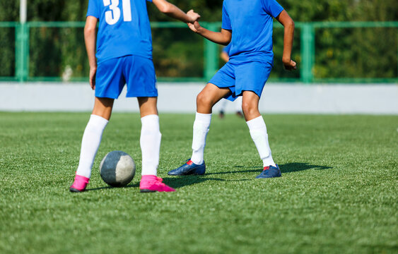 Young sport boys in blue sportswear running and kicking a  ball on pitch. Soccer youth team plays football in summer. Activities for kids, training	