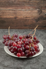 White plate of red delicious grapes on marble table