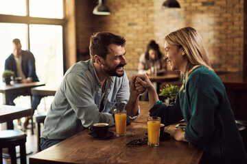 Happy couple holding hands and talking in a cafe.