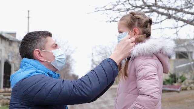 The father puts a surgical masks on his daughter is face on the street.  Concept of coronavirus COVID-19. 