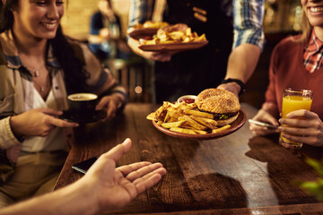 Close-up of waiter serving hamburger with French fries in a pub.