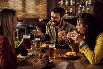Cheerful friends talking while drinking beer and eating in a pub.