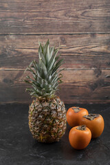 Photo of ripe juicy pineapple and persimmons on black surface
