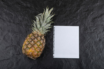 Photo of ripe juicy pineapple and empty paper on black surface