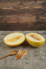 Halved delicious yellow melons on marble surface with wooden spoon aside