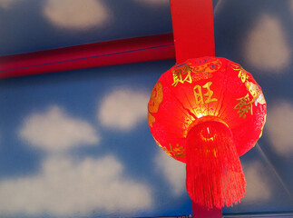 A red lantern hanging on a wooden beam painted in red. Behind the scenes, spraying an airbrush is a picture of white sky and clouds.