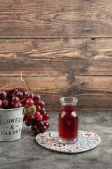 Metal bucket of red fresh grapes and glass of juice on marble table