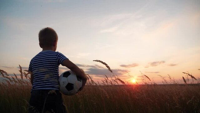Childhood dream. boy holding soccer ball walking in the park silhouette. happy family kid dream concept. kid boy walking on the field silhouette at sunset fun carries a soccer ball. baby winner