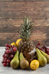 Ripe pineapple in wooden box with various fresh fruits on marble surface