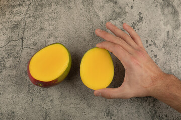 Fototapeta na wymiar Male hand holding slice of mango on marble surface