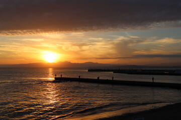 Fototapeta na wymiar 片瀬江ノ島海岸から見る伊豆半島に沈むオレンジ色の夕日と堤防のシルエット