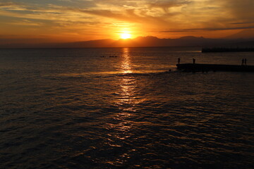 Fototapeta na wymiar 片瀬江ノ島海岸から見る伊豆半島に沈むオレンジ色の夕日と堤防のシルエット