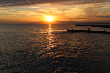 片瀬江ノ島海岸から見る伊豆半島に沈むオレンジ色の夕日と堤防のシルエット