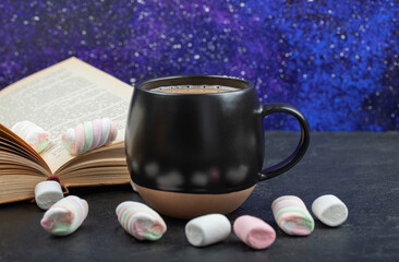Cup of aromatic coffee with open book and marshmallows on blue background