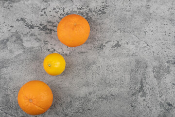Two fresh orange fruits with whole lemon on stone table