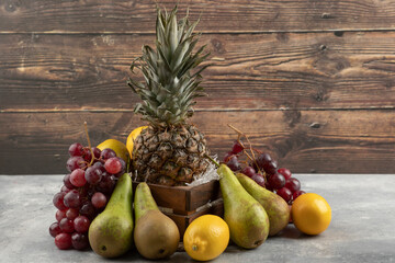 Ripe pineapple in wooden box with various fresh fruits on marble surface - Powered by Adobe