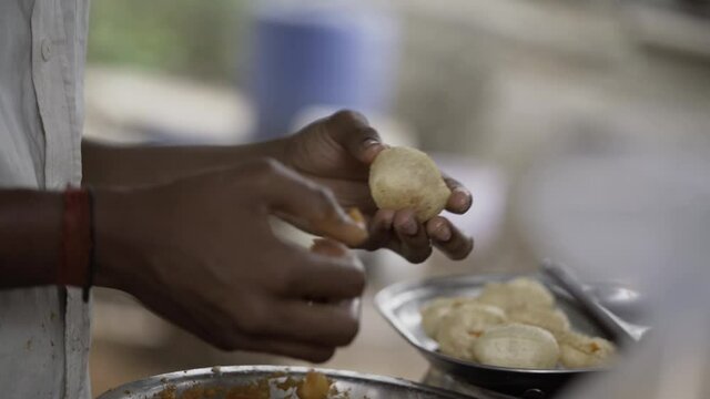 Close up of a street food recipe made with small puri balls filled with spiced and mashed aloo and specially made spiced water. A boy preparing panipuri in the streets of India.
