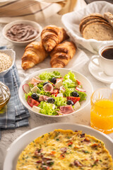 Broad assortment of food including omelette, croissants, salad, bread, oatmeal, jam, waffles, honey, choclate spread, coffee and orange juice served on a table