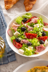 Healthy salad in a bowl with olives, raddishes, tomato, cheese and lean ham served for breakfast