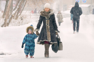 A woman and a child walk in the winter snowfall.
