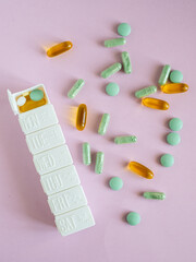 Different pharmaceutical medicine pills, tablets and white pill case on pink background. Health care. Top view. Pharmaceutical picture. 