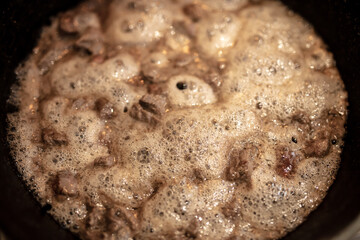 Meat in foam is fried in a pan.