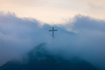 Fototapeta na wymiar A single cross stands on a mountain engulfed in white clouds